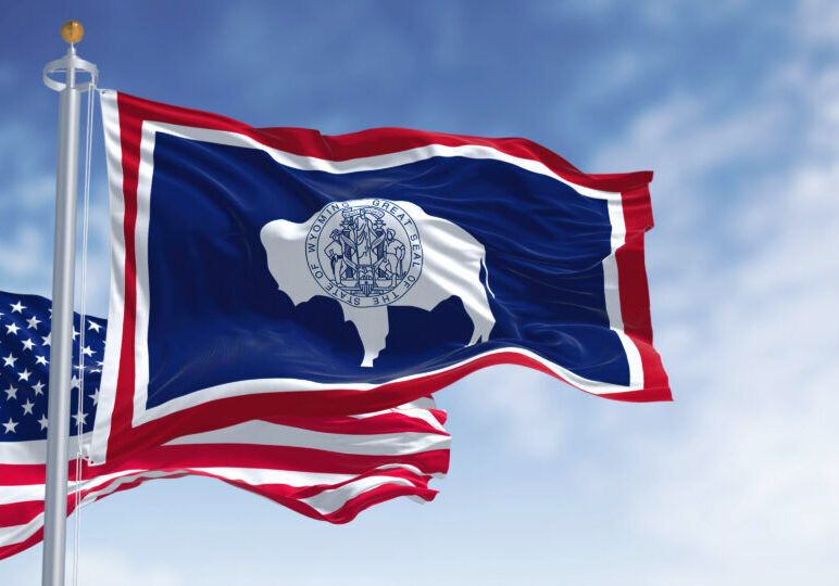 The Wyoming state flag waving along with the national flag of the United States of America. Wyoming is a state in the Mountain West subregion of the Western United States